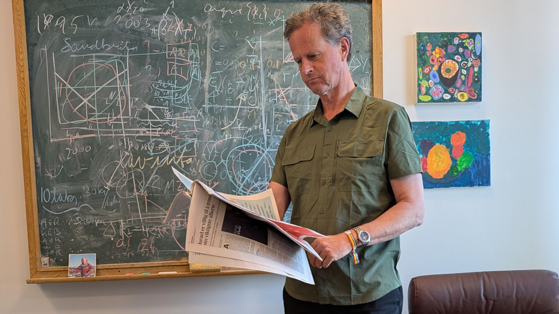 Professor med avis, foran tavle.